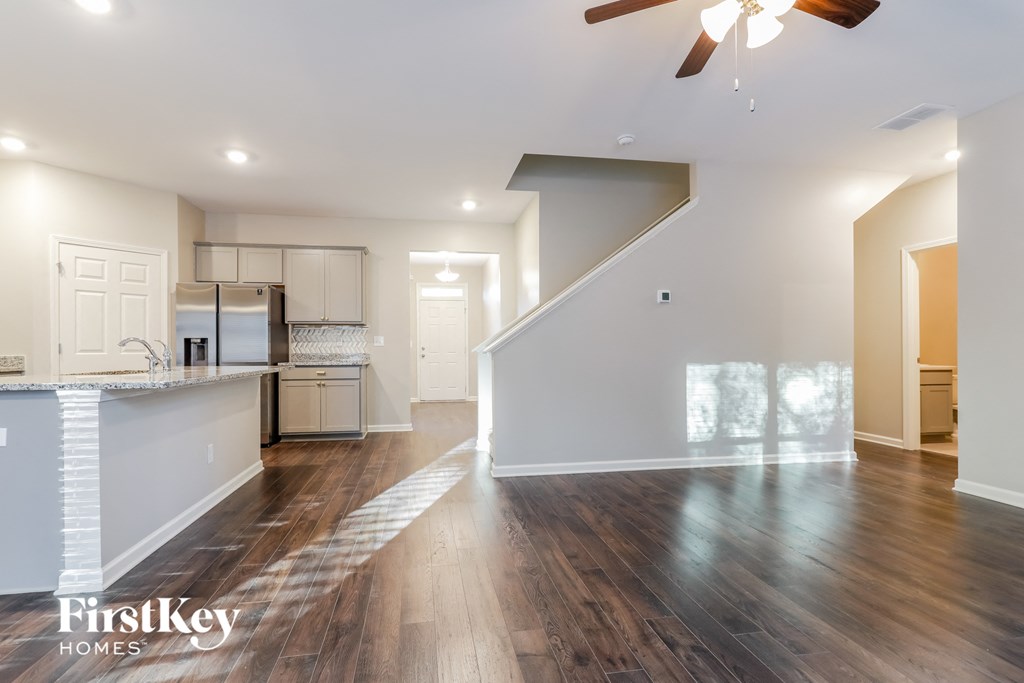 an empty living room with a kitchen and a ceiling fan