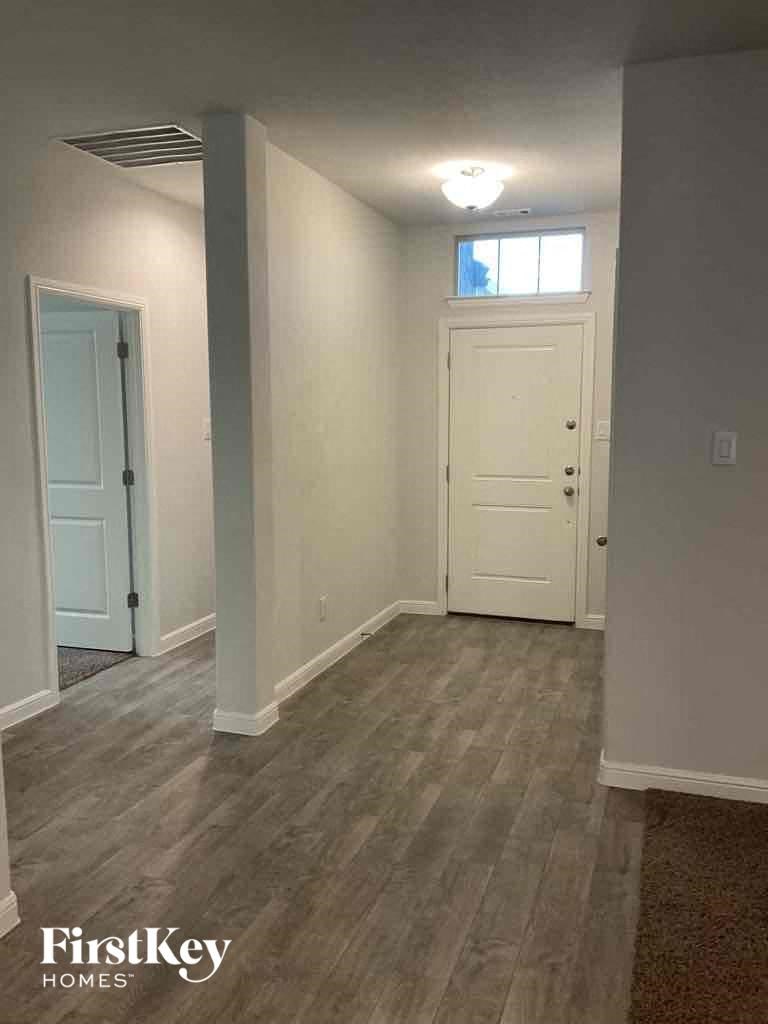 A room with a light grey floor and white walls with a door on the left and a window on the right.