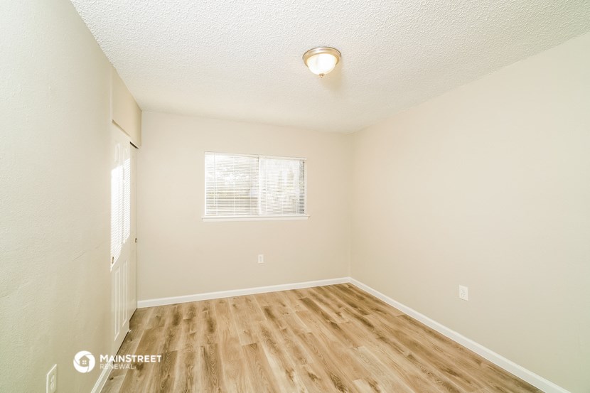 a spacious bedroom with hardwood flooring and a window