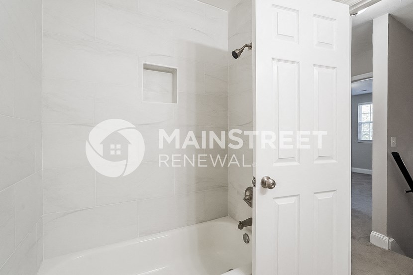 a renovated bathroom with white tiles and a shower and a white door