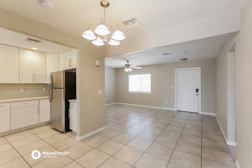 an empty kitchen and living room with white cabinets and a refrigerator
