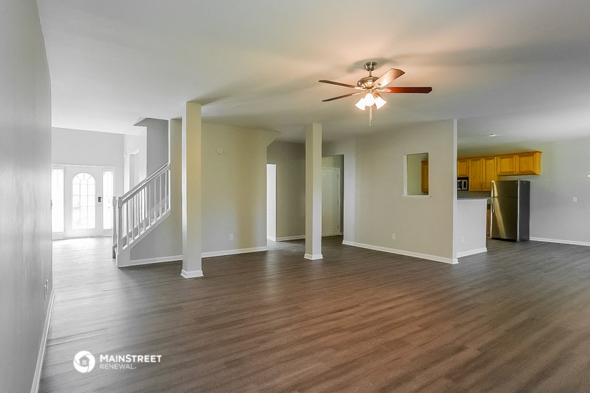 an empty living room with a ceiling fan and a kitchen