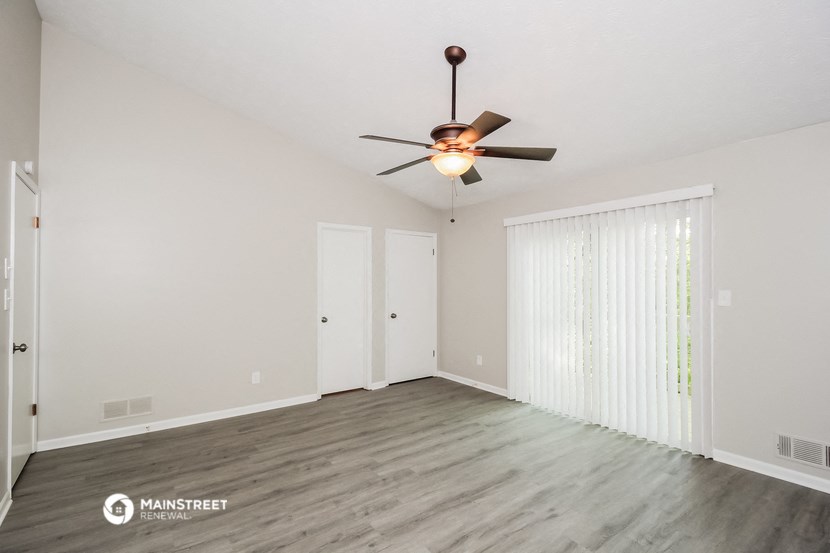 a spacious living room with white walls and a ceiling fan
