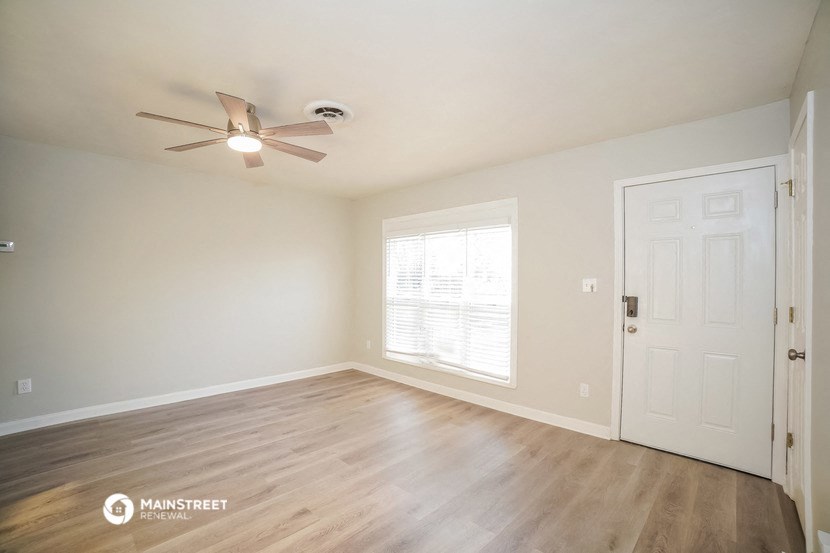 the spacious living room with wood flooring and a ceiling fan