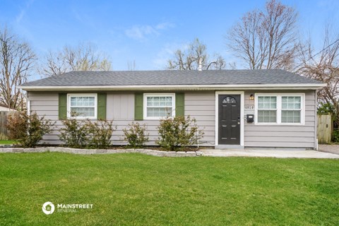 a small gray house with green trim and a black door
