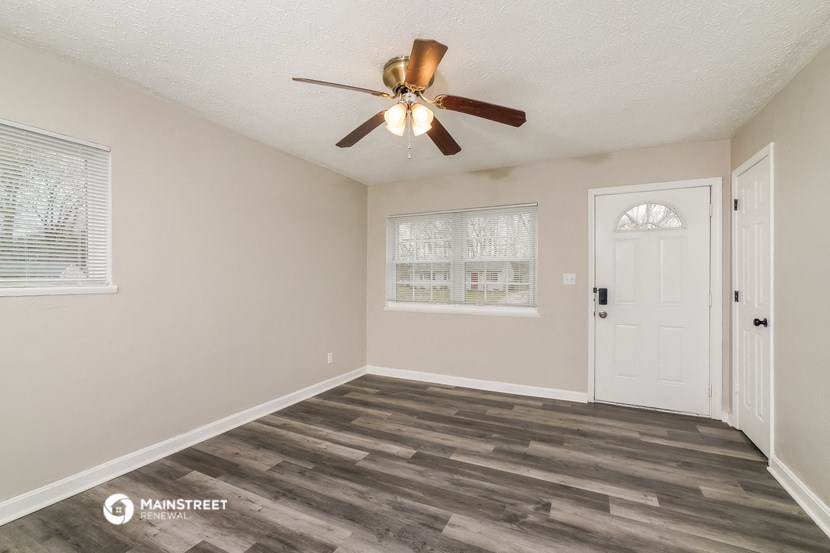 the spacious living room with a ceiling fan and a white door