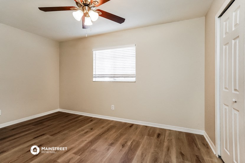 the spacious living room of this home has a ceiling fan and wood flooring