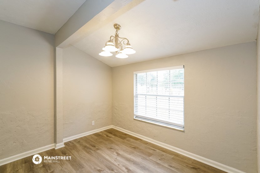 the spacious living room of a home with wood flooring and a window