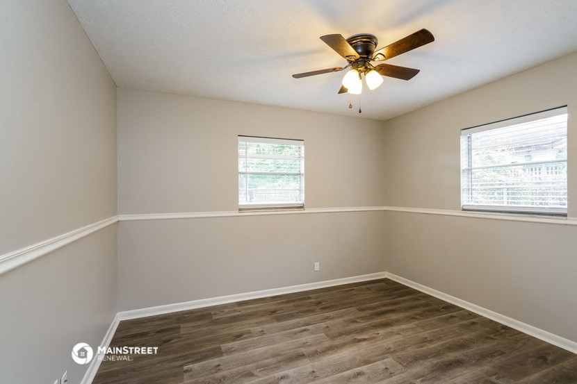 an empty room with a ceiling fan and two windows