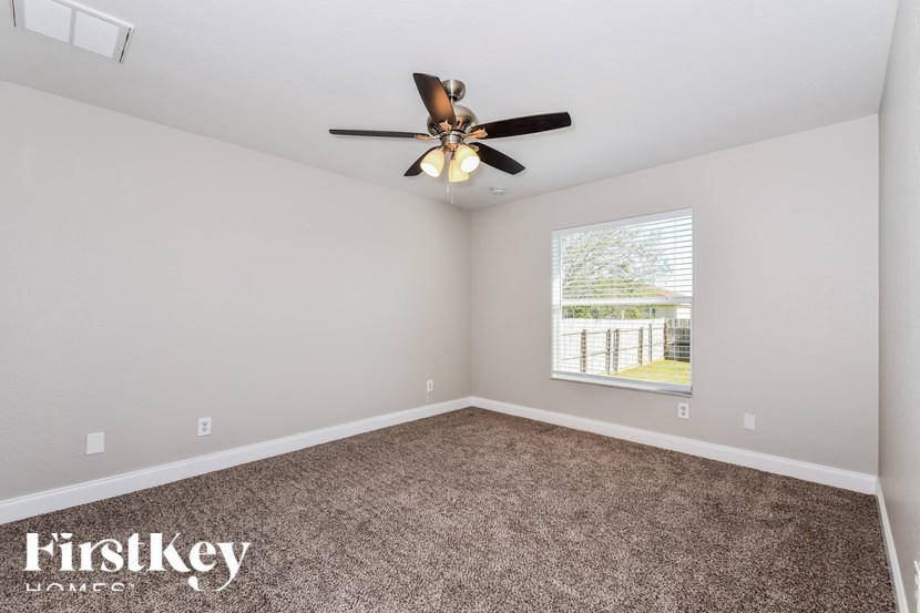 A room with a ceiling fan and a window with a view of a fence and trees.