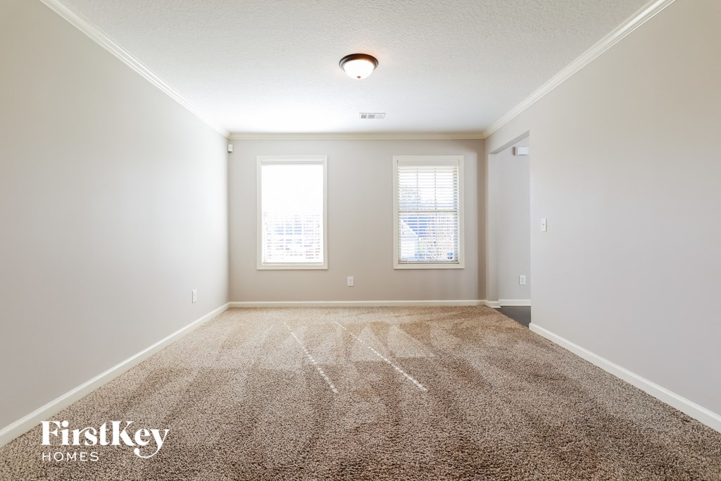 a spacious living room with carpet and two windows