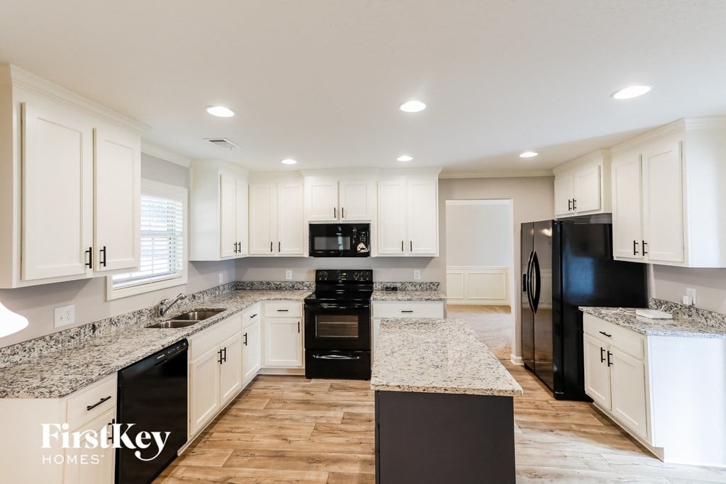 a white kitchen with marble counter tops and black appliances