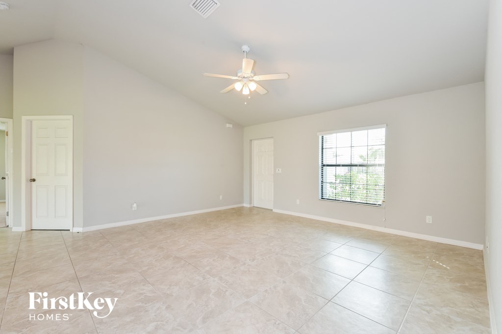 A spacious empty room with a ceiling fan and a window.