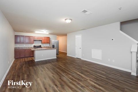 A spacious living room with wooden floors and a kitchen area in the background.