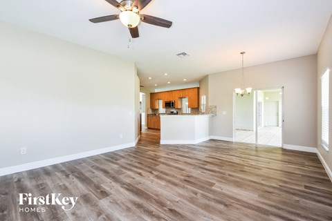 an empty living room with a ceiling fan and a kitchen