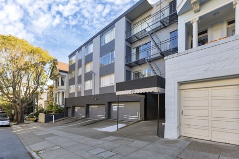 A modern apartment building with a garage door and a tree in front.