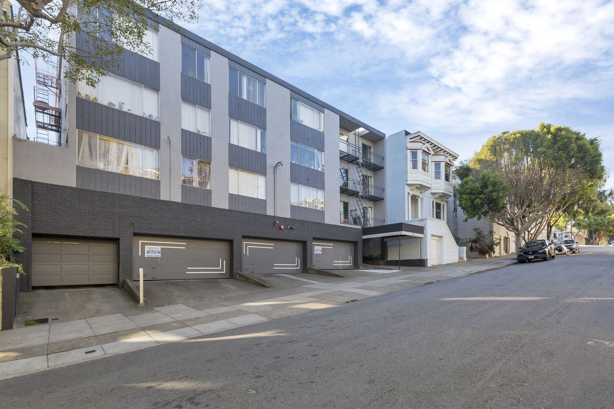 A street view of a residential area with apartment buildings and cars parked on the side of the road.