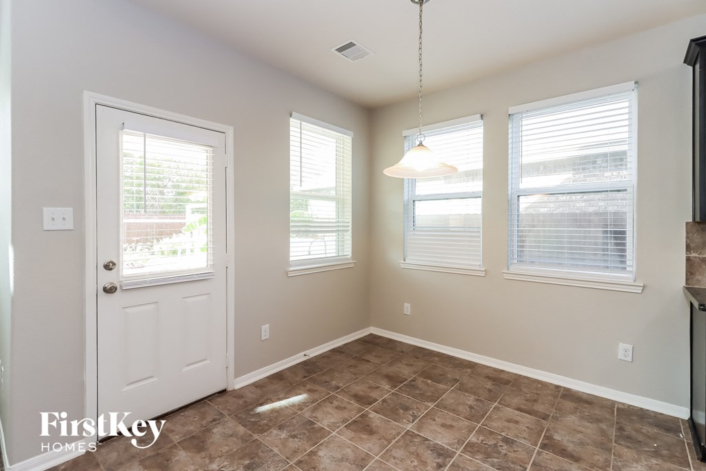 an empty dining room with a white door and three windows