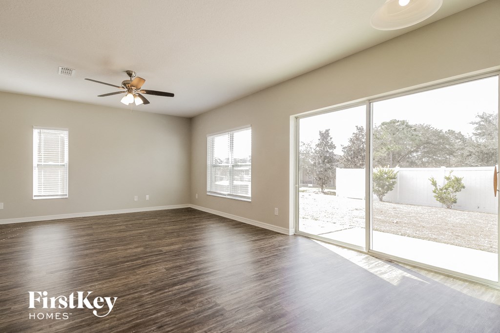 A spacious room with a ceiling fan and sliding glass doors leading to a backyard.