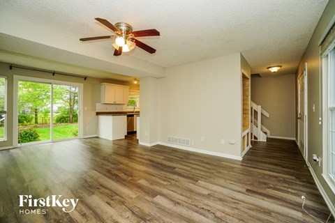 an empty living room with a ceiling fan and a kitchen