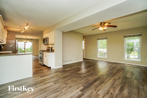 an empty living room with a kitchen and a ceiling fan