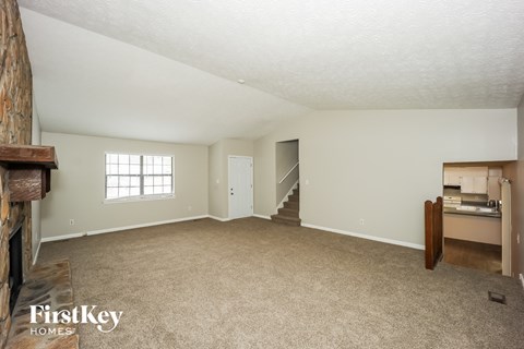 A spacious room with a carpeted floor and a fireplace on the left side.