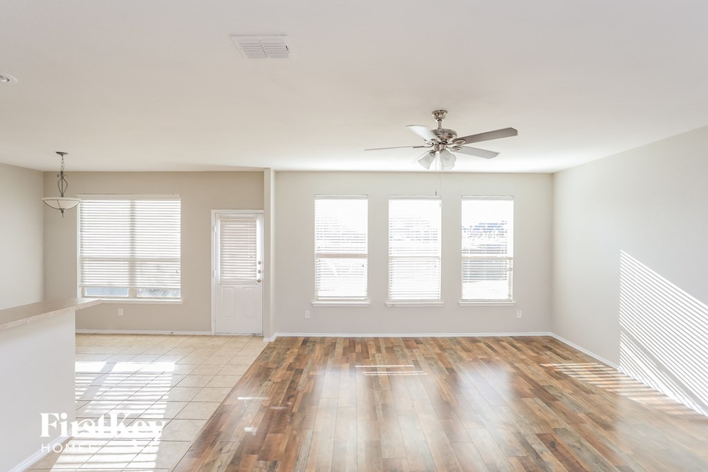 an empty living room with a ceiling fan and windows