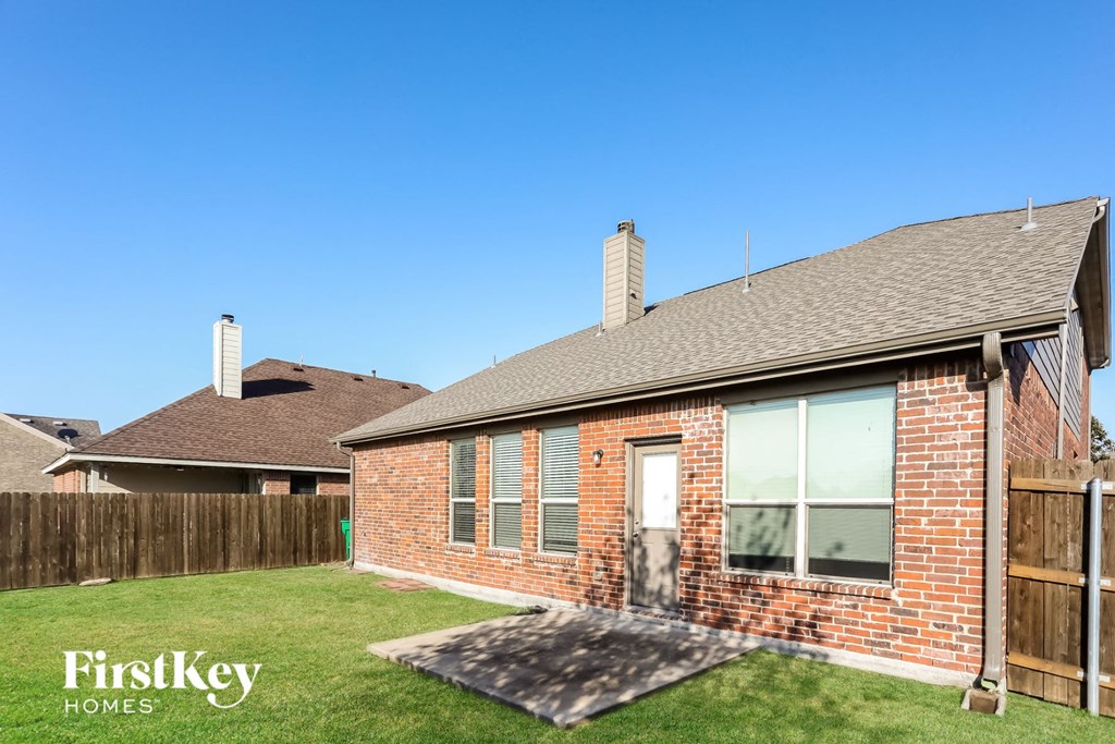 the backyard of a brick house with a lawn and a wooden fence
