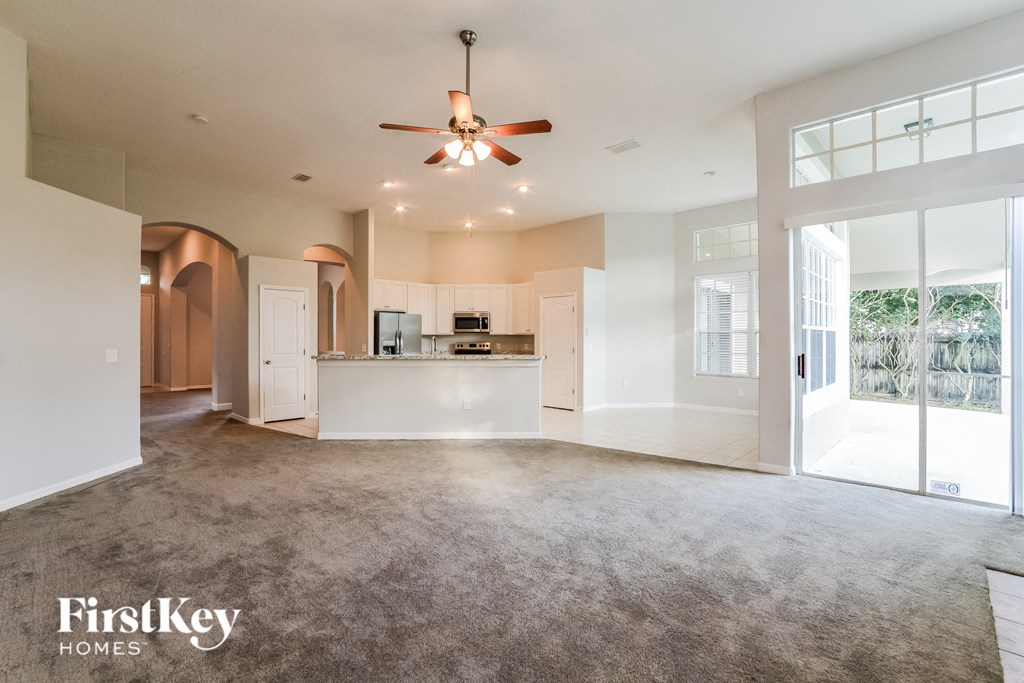 A spacious living room with a kitchen in the background and a ceiling fan above.