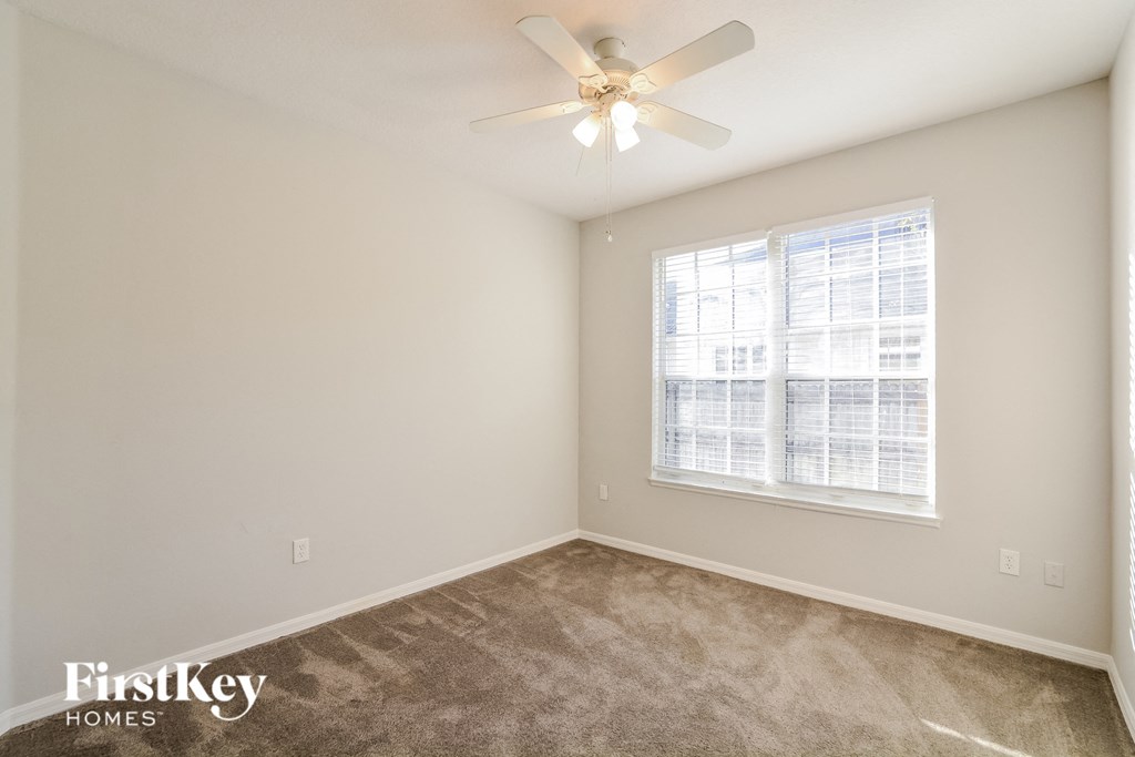 A room with a carpet floor, a ceiling fan, and a window with blinds.