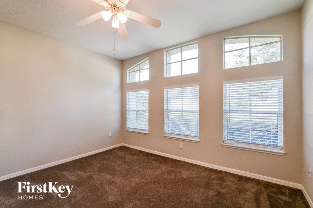 A room with a carpeted floor, a ceiling fan, and three windows with blinds.