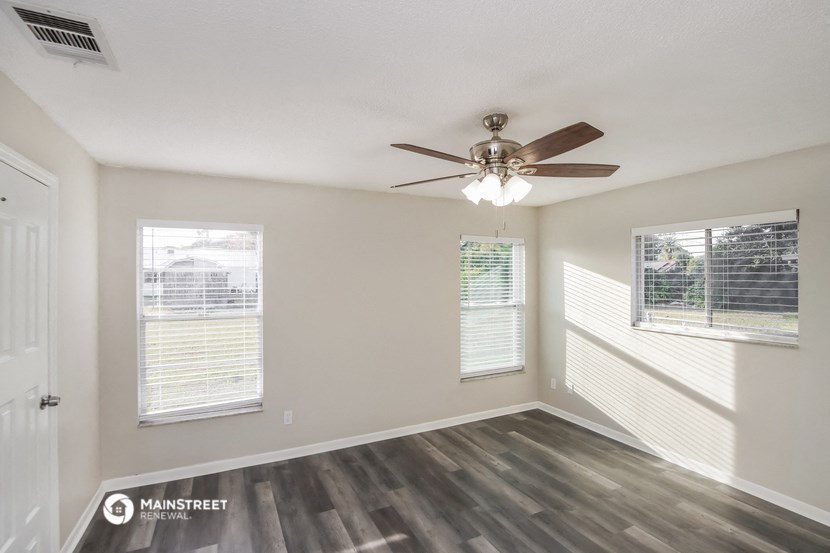 an empty living room with a ceiling fan and two windows