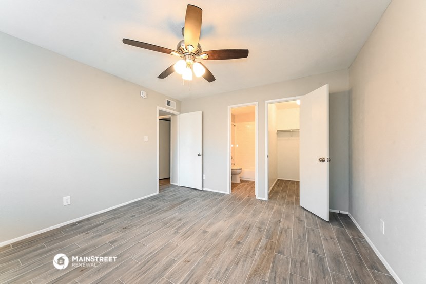 the spacious living room with wood flooring and a ceiling fan