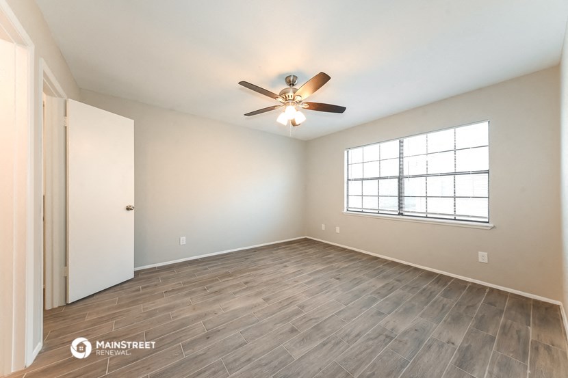 the spacious living room with wood flooring and a ceiling fan