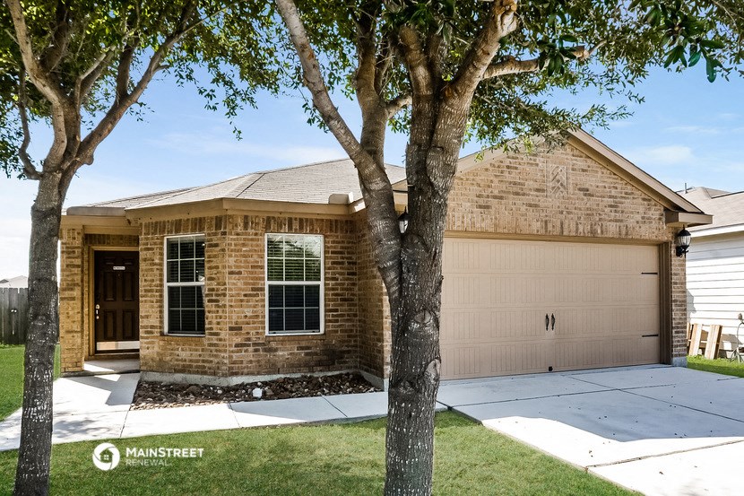 a tan brick house with a garage door and two trees