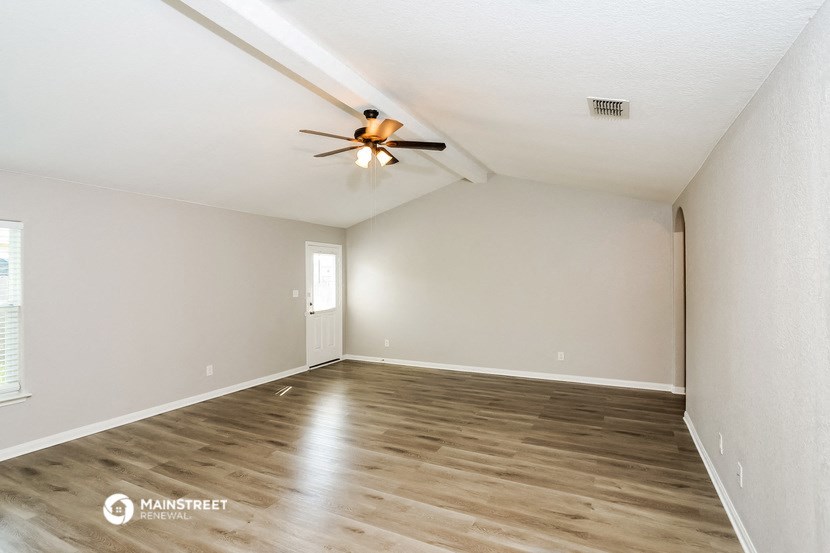 the spacious living room with wood flooring and a ceiling fan
