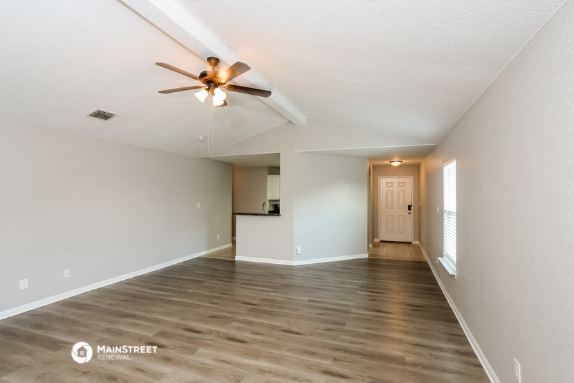 an empty living room with a ceiling fan and a kitchen