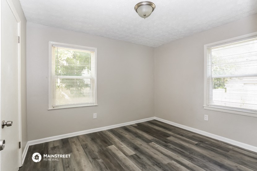 the interior of a bedroom with wood flooring and two windows
