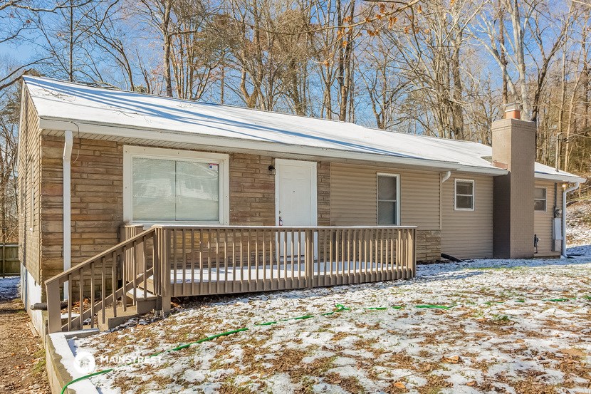 a small brown house with a porch with snow on the ground