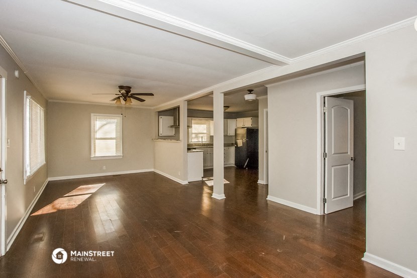 an empty living room with a ceiling fan and a kitchen