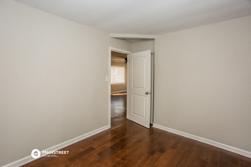 a bedroom with white walls and wood flooring and a door to a room with