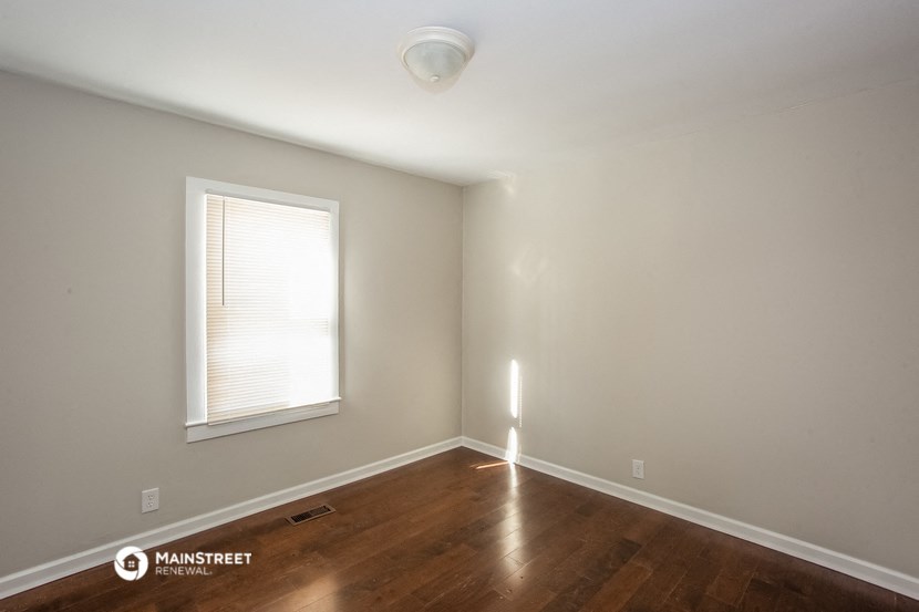 a bedroom with wood floors and a window and white walls