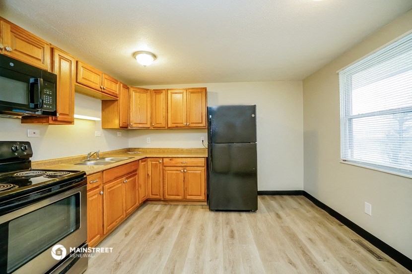 an empty kitchen with wooden cabinets and a black refrigerator
