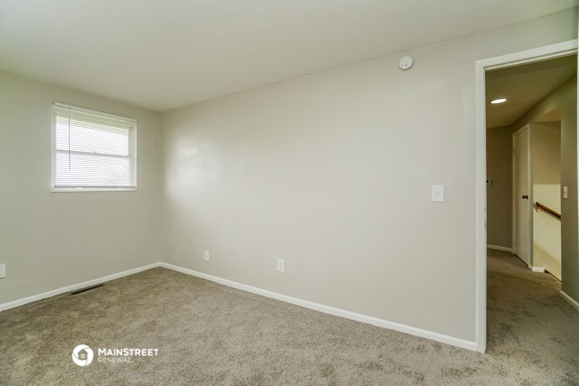 the bedroom of an apartment with carpet and a door to the hallway