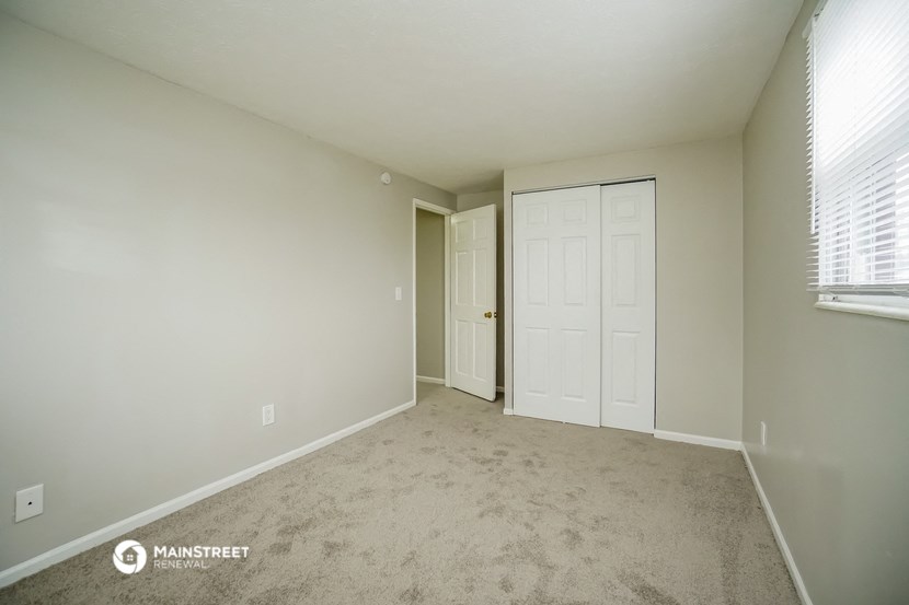 the spacious living room of an apartment with a carpeted floor and a white door