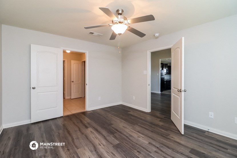 an empty living room with a ceiling fan and a door to a hallway