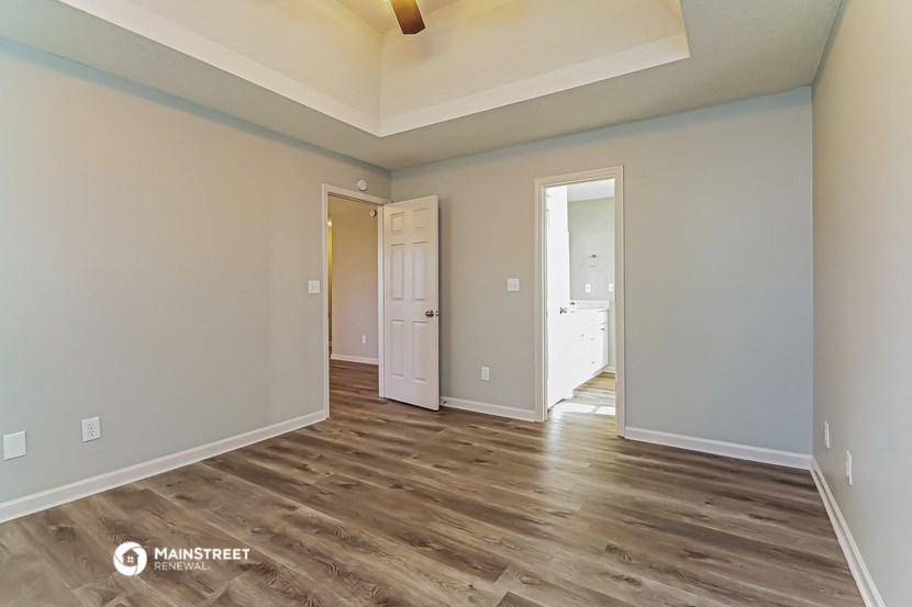 the spacious living room with wood flooring and an open door to the bedroom