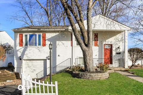 a white house with a red door and a tree in the front yard