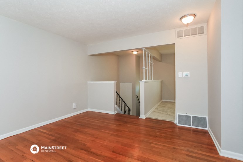the living room of an apartment with wood flooring and a staircase
