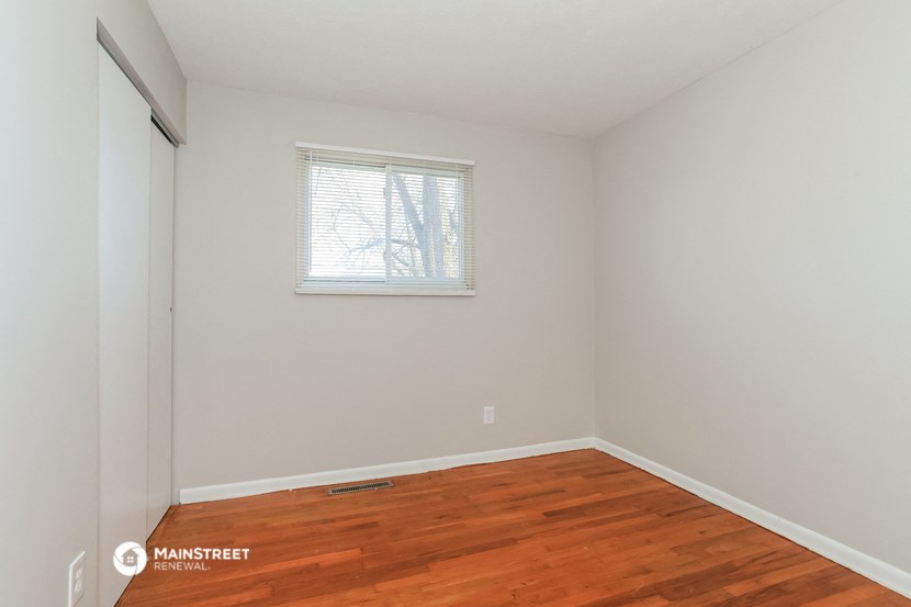 a bedroom with white walls and wood flooring and a window